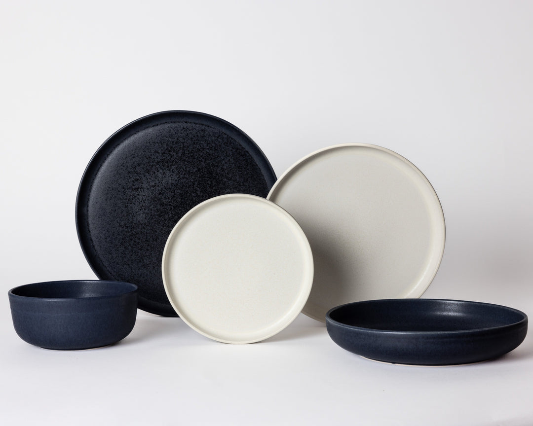 Serviesset van Mimo Homeware in wit en donkerblauw keramiek, bestaande uit borden en kommen.